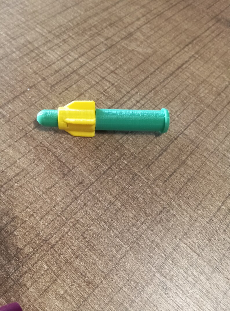 Puede incluir: Un misil de juguete de pl&aacute;stico verde y amarillo con una punta puntiaguda y una parte posterior redondeada.