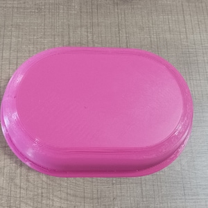 Puede incluir: Una bandeja ovalada de color rosa con una superficie lisa.