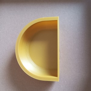 May include: A yellow half-circle shaped ceramic planter. The planter has a smooth, rounded surface and a slightly raised lip around the edge.