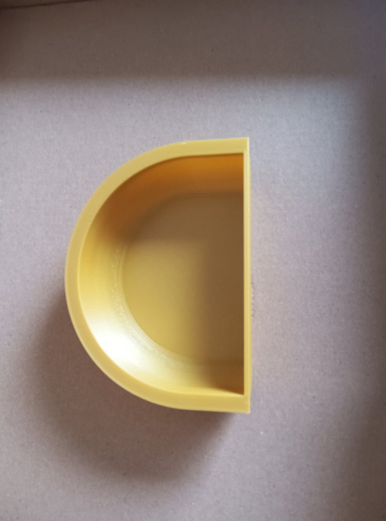 May include: A yellow half-circle shaped ceramic planter. The planter has a smooth, rounded surface and a slightly raised lip around the edge.