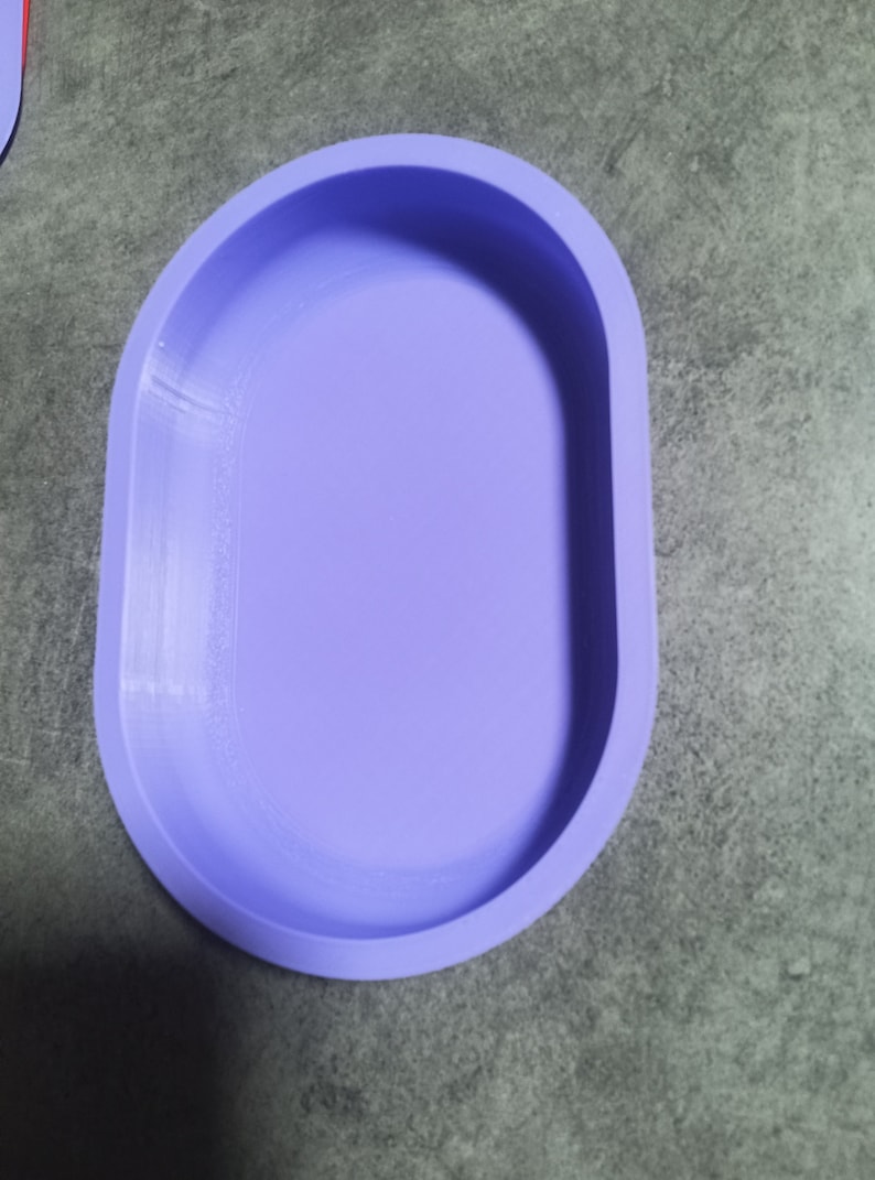 Puede incluir: Un plato ovalado de color lila claro con una superficie lisa ligeramente texturizada. El plato est&aacute; hecho de un material suave y flexible, posiblemente silicona.