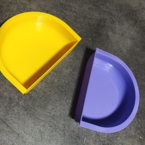 May include: Two half-circle shaped containers, one yellow and one purple. The containers are made of a smooth, plastic-like material.