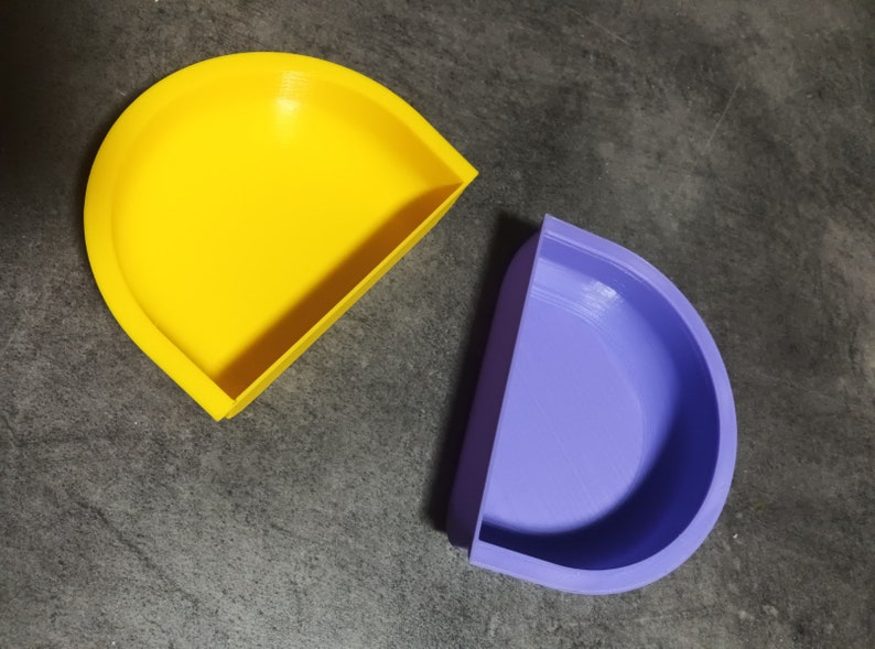 May include: Two half-circle shaped containers, one yellow and one purple. The containers are made of a smooth, plastic-like material.
