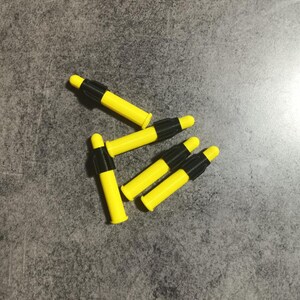 Puede incluir: Cinco dardos amarillos y negros con puntas negras. Los dardos est&aacute;n dispuestos en un grupo sobre una superficie gris.