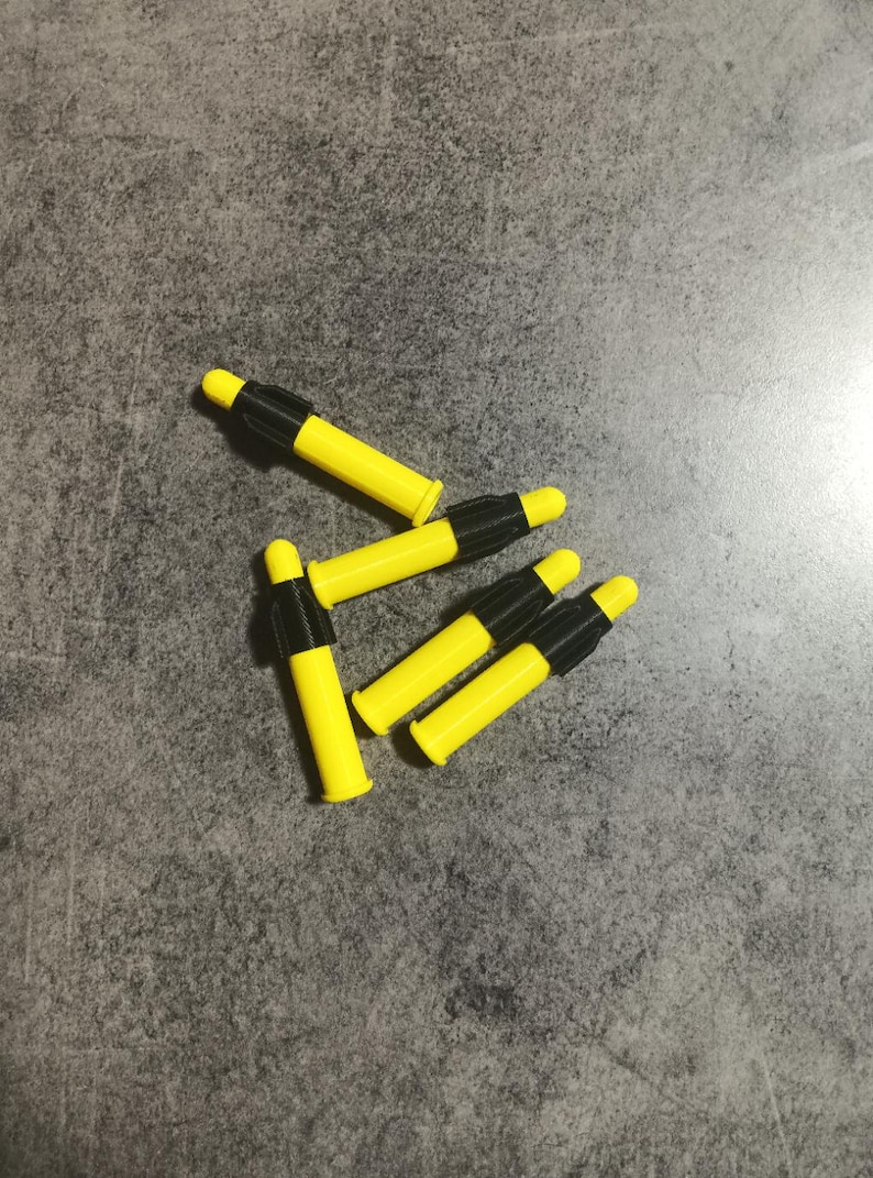 Puede incluir: Cinco dardos amarillos y negros con puntas negras. Los dardos est&aacute;n dispuestos en un grupo sobre una superficie gris.