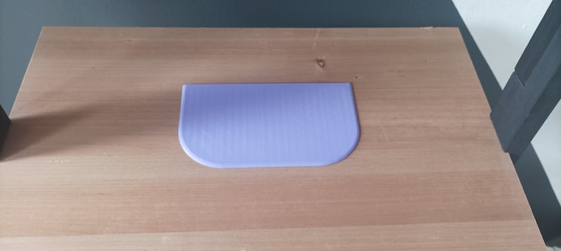 May include: A light purple plastic scraper with a rounded edge, sitting on a wooden surface.