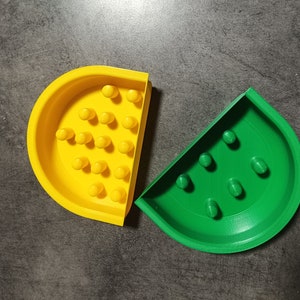 May include: Two half-circle shaped slow feeder bowls for pets. One bowl is yellow with 20 small indentations and the other is green with 7 indentations.