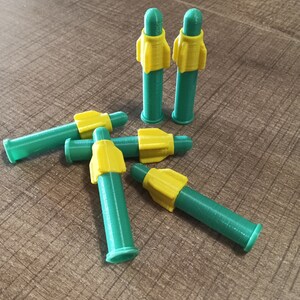 Puede incluir: Cinco puntas de dardos de pl&aacute;stico verde y amarillo. Las puntas tienen forma de cohete y tienen una punta amarilla y un cuerpo verde.