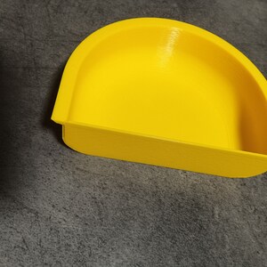 May include: A bright yellow plastic dish with a curved, rounded shape. The dish is designed to hold small items.