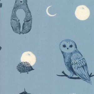 May include: Blue fabric with a repeating pattern of woodland animals and celestial elements. The design includes a bear, an owl on a branch, a hedgehog, a crescent moon, and full moons. The illustrations are in a detailed, vintage style.