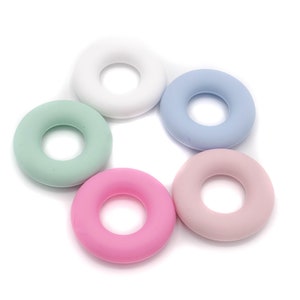 May include: Five silicone rings in different colors: white, light blue, light green, pink, and light pink. The rings are all the same size and shape, and they are arranged in a circle.