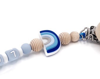 Può includere: Un mordedor arcobaleno in silicone blu e bianco con perline di legno e un clip. Il mordedor ha i numeri 0 e 1.