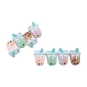Könnte beinhalten: Sechs Silikon-Bubble-Tea-Anhänger in verschiedenen Farben, darunter rosa, grün, braun und lila. Jeder Anhänger hat einen Strohhalm und Boba-Perlen.