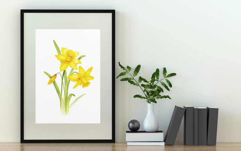 Pode incluir: Uma pintura de aquarela emoldurada de narcisos amarelos com caules e folhas verdes sobre um fundo branco.