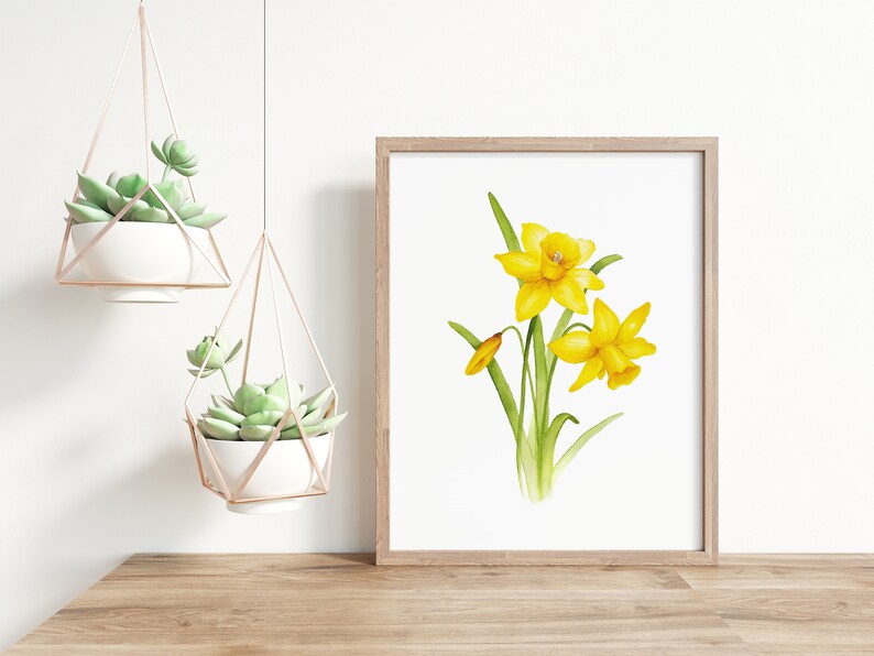 Pode incluir: Uma pintura em aquarela de narcisos amarelos com folhas verdes sobre um fundo branco. A pintura &eacute; emoldurada em uma moldura de madeira clara.