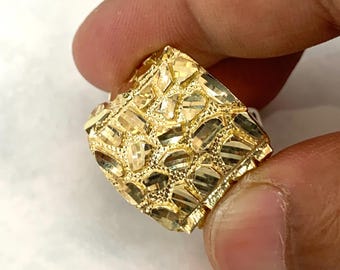 May include: A gold ring with a textured, diamond-cut design. The ring is wide and has a square shape.