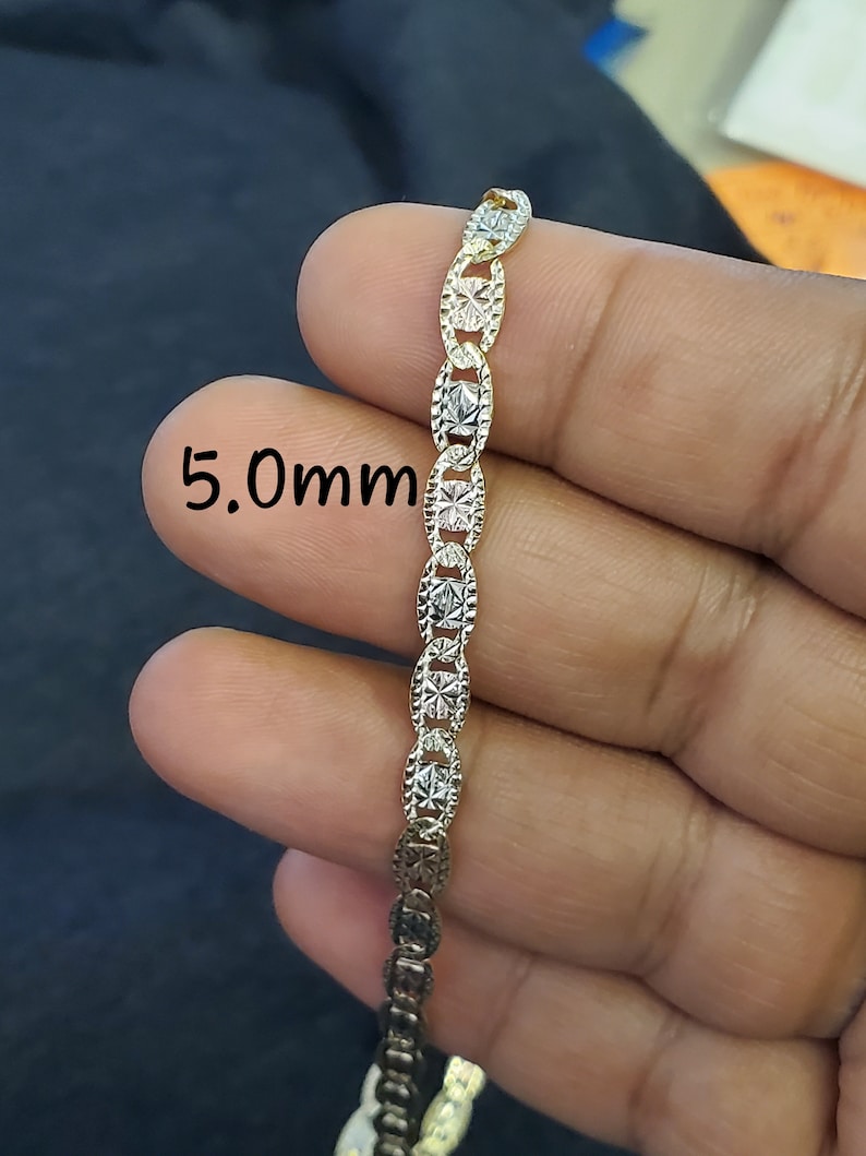 May include: A two-tone gold chain necklace with a 5.0mm width. The chain is made of oval links with a diamond-cut design.