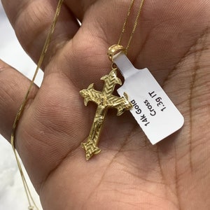 May include: A gold chain necklace with a detailed gold cross pendant. The pendant has a small figure of Jesus on the cross. The tag attached to the necklace reads "14k Gold Cross 1.3g 11"