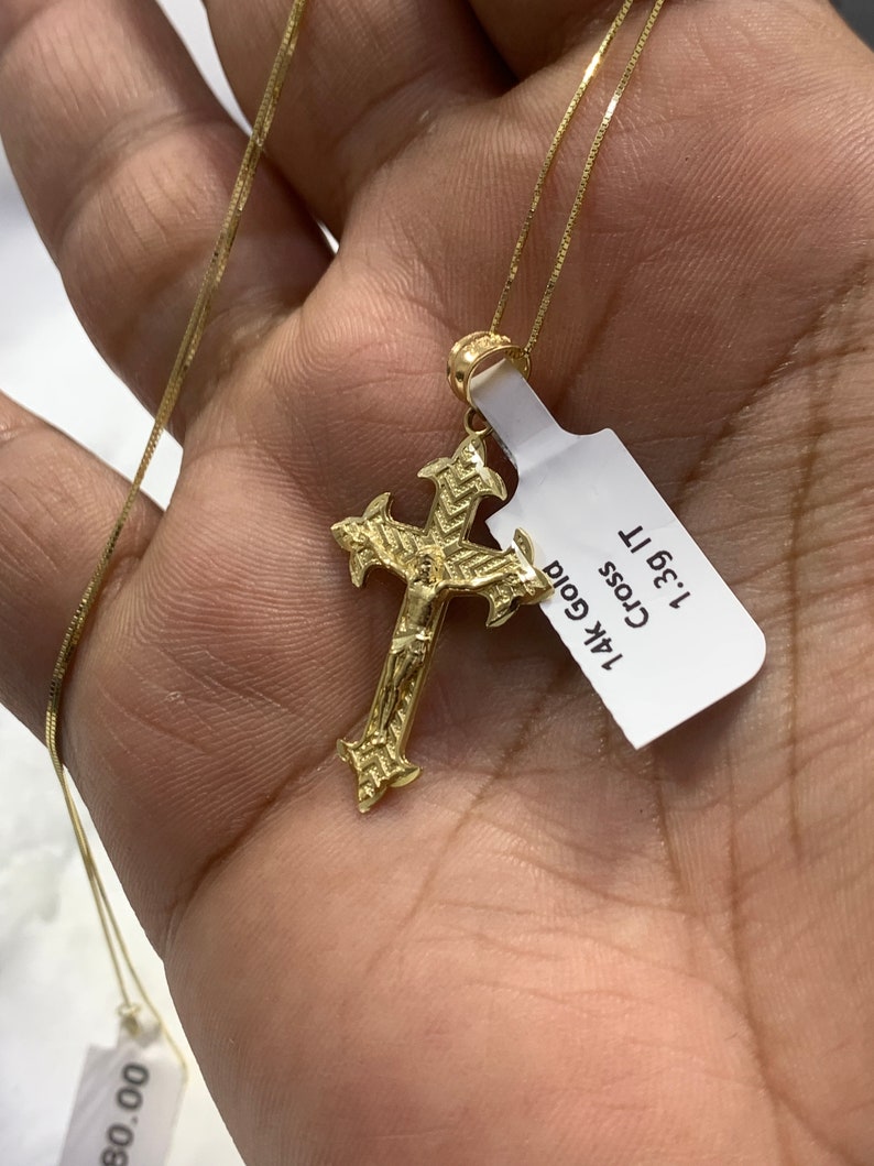 May include: A gold chain necklace with a detailed gold cross pendant. The pendant has a small figure of Jesus on the cross. The tag attached to the necklace reads "14k Gold Cross 1.3g 11"