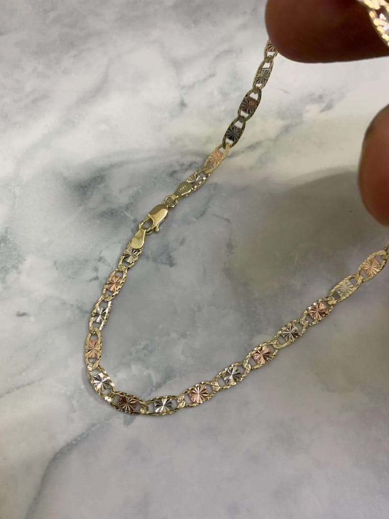 K&ouml;nnte beinhalten: Eine goldene Kettenkette mit einem Ankerketten-Design. Die Kette besteht aus drei verschiedenen Goldfarben: Gelb, Wei&szlig; und Rotgold.