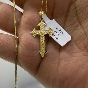 May include: A gold chain necklace with a detailed gold cross pendant. The pendant is 1.36" tall and has a figure of Jesus on it. The tag attached to the pendant reads "14k Gold Cross 1.36" "