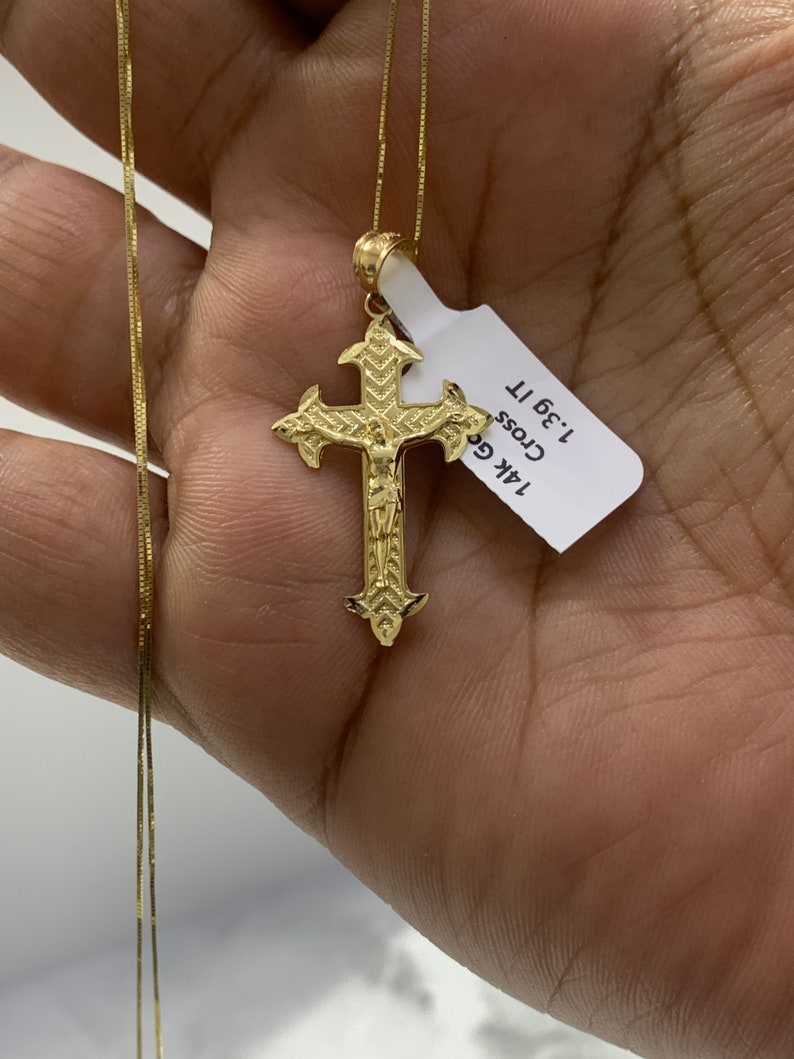 May include: A gold chain necklace with a detailed gold cross pendant. The pendant is 1.36" tall and has a figure of Jesus on it. The tag attached to the pendant reads "14k Gold Cross 1.36" "