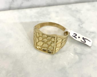 May include: A gold ring with a square face and a textured design. The ring is size 2.5.
