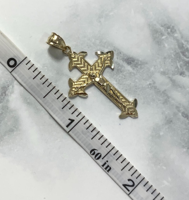 May include: A gold-toned cross pendant with a detailed design and a figure of Jesus Christ. The pendant is approximately 1 inch in length.