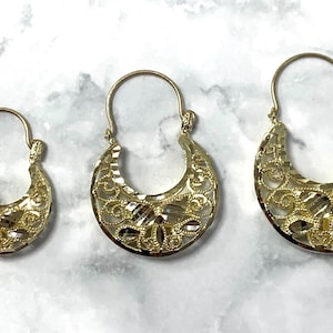 May include: Three pairs of gold hoop earrings with intricate filigree designs. The earrings are different sizes, with the largest pair being the most ornate.