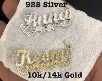 May include: Two personalized name necklaces, one in silver and one in gold. The silver necklace says "Anna" and the gold necklace says "Keona". The necklaces are on a white background.