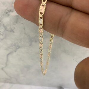 K&ouml;nnte beinhalten: Eine goldene Kettenkette mit einem Ankerketten-Design. Die Kette besteht aus drei verschiedenen Goldfarben: Gelb, Wei&szlig; und Rotgold.