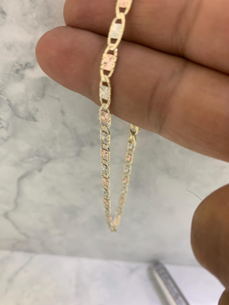 K&ouml;nnte beinhalten: Eine goldene Kettenkette mit einem Ankerketten-Design. Die Kette besteht aus drei verschiedenen Goldfarben: Gelb, Wei&szlig; und Rotgold.