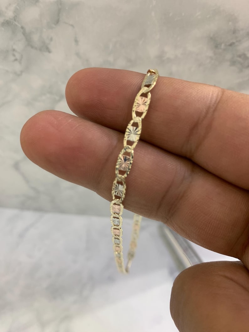 K&ouml;nnte beinhalten: Ein goldenes Kettenarmband mit dreifarbigem Design. Die Kette besteht aus Gelb-, Wei&szlig;- und Ros&eacute;gold.
