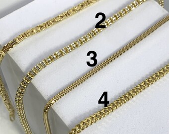 May include: Four gold chains on a white surface. The chains are numbered 1 through 4. Chain 1 is a thick, braided chain. Chain 2 is a thin chain with small, clear stones. Chain 3 is a thin, snake chain. Chain 4 is a thin, braided chain.