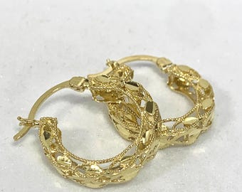 May include: A pair of gold hoop earrings with a delicate, intricate design. The earrings are made of a thin, woven metal and have a slightly oval shape.