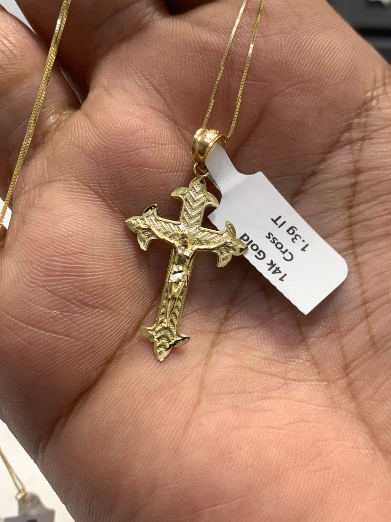 May include: A gold chain necklace with a detailed gold cross pendant. The tag attached to the chain reads "14k Gold Cross 1.3g 1T".