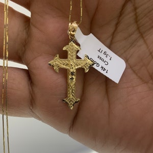 May include: A gold chain necklace with a detailed gold cross pendant. The pendant features a figure of Jesus Christ. The tag attached to the necklace reads "14k Gold Cross 1.3g 1T".