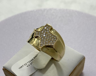 May include: A gold-colored ring featuring a detailed outline of the state of Texas, encrusted with small, sparkling stones. The ring is displayed on a white surface, with a tag that reads "10KT CZ TEXAS RING 4.0 DT".