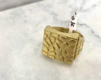 May include: A gold ring with a square face featuring a textured, geometric pattern.