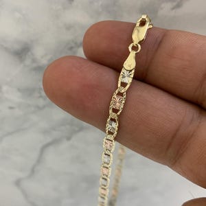 K&ouml;nnte beinhalten: Eine goldene Kettenkette mit dreifarbigem Design. Die Kette besteht aus Gelb-, Wei&szlig;- und Ros&eacute;gold. Die Kette ist im Curb-Stil mit einer Diamant-Schliff-Oberfl&auml;che.