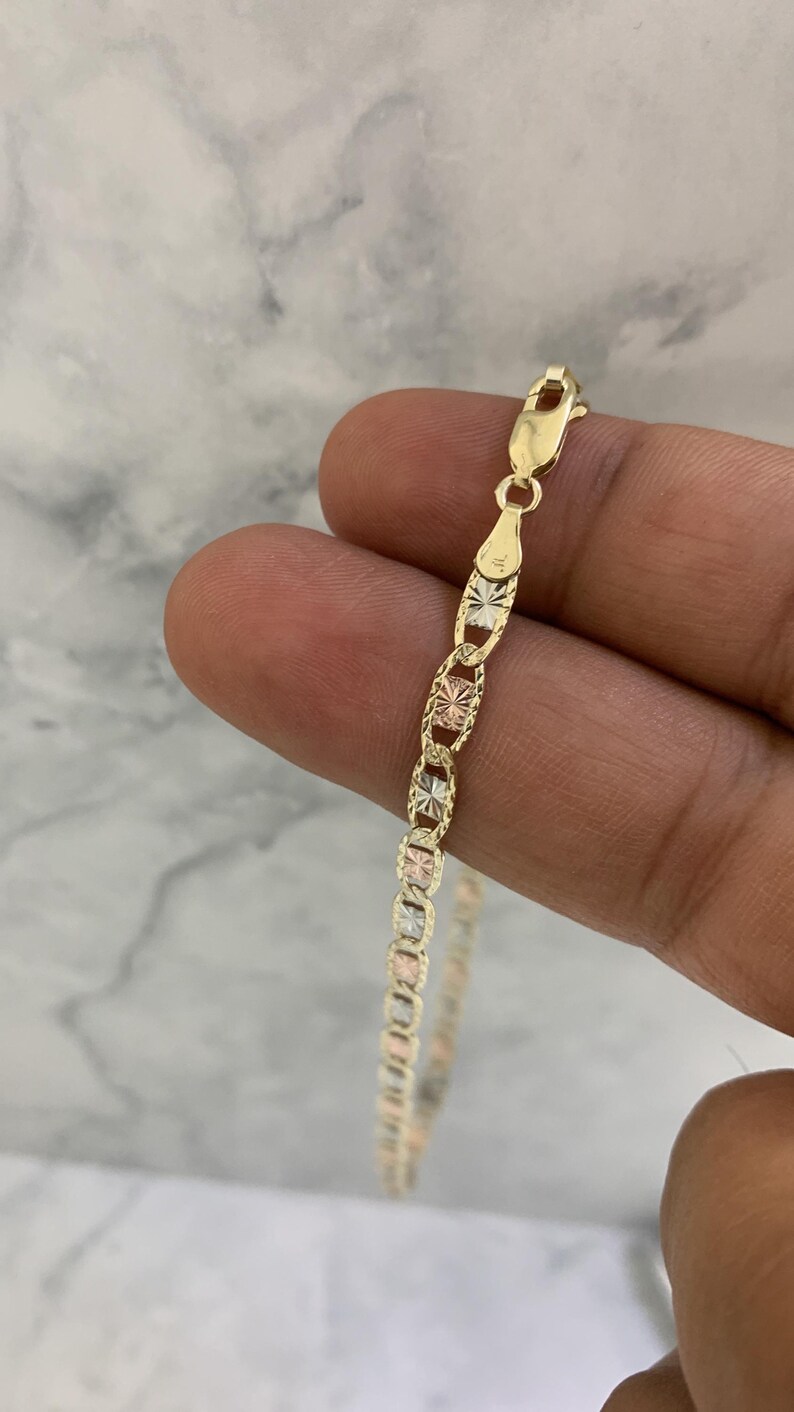 K&ouml;nnte beinhalten: Eine goldene Kettenkette mit dreifarbigem Design. Die Kette besteht aus Gelb-, Wei&szlig;- und Ros&eacute;gold. Die Kette ist im Curb-Stil mit einer Diamant-Schliff-Oberfl&auml;che.