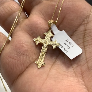 May include: A gold chain necklace with a detailed gold cross pendant. The tag attached to the chain reads "14K Gold Cross 1.3g 11"