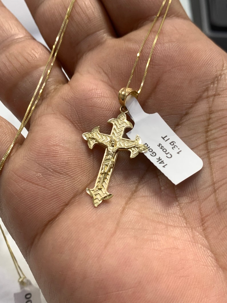 May include: A gold chain necklace with a detailed gold cross pendant. The tag attached to the chain reads "14K Gold Cross 1.3g 11"