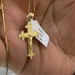 May include: A gold chain necklace with a detailed gold cross pendant. The pendant features a figure of Jesus Christ. The tag attached to the chain reads "14K Gold Cross 1.3g 1T."