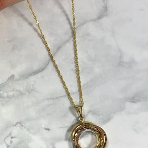 May include: A gold chain necklace with a pendant featuring three interlocking circles in different shades of gold.