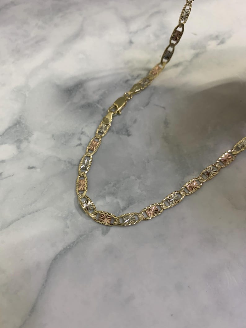 K&ouml;nnte beinhalten: Eine goldene Kettenkette mit dreifarbigem Design. Die Kette besteht aus drei verschiedenen Goldfarben: Gelb, Wei&szlig; und Rotgold.