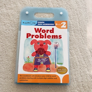 May include: A blue and white workbook with the title "Word Problems" and a cartoon pig wearing a basketball uniform. The book is part of the Kumon Math Workbooks series for Grade 2. The book cover also includes the text "Aligned to State Math Standards".