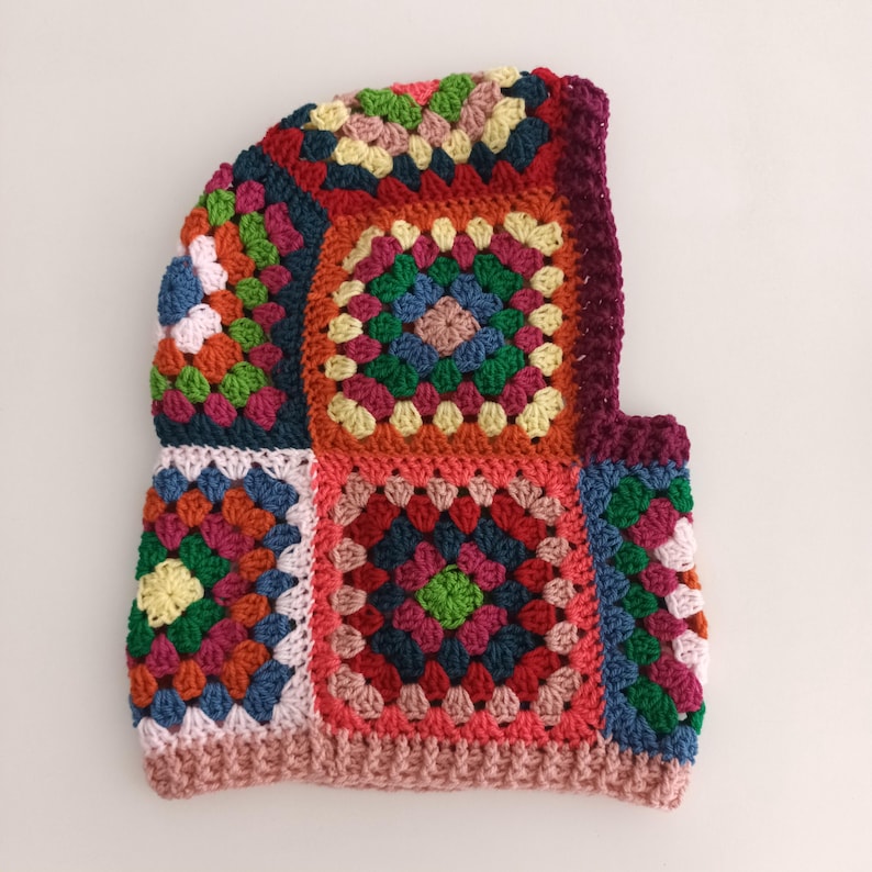 May include: A colourful crocheted hat with a hood, made with granny squares in shades of red, orange, yellow, green, blue, and pink.