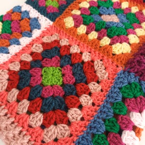 May include: A colourful crocheted blanket featuring a variety of squares in shades of pink, red, green, blue and yellow.