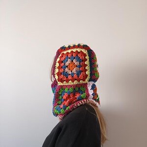 May include: A colourful crocheted hooded neck warmer with a granny square pattern in shades of red, orange, yellow, green, blue, and white.